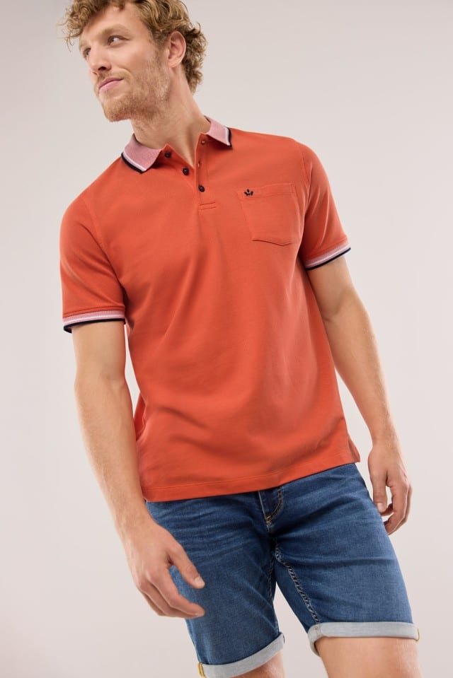 Ein Mann trägt ein Pique-Polo Hitzefrei mit in Uni Orange, dazu blaue Jogger-Jeans Shorts.