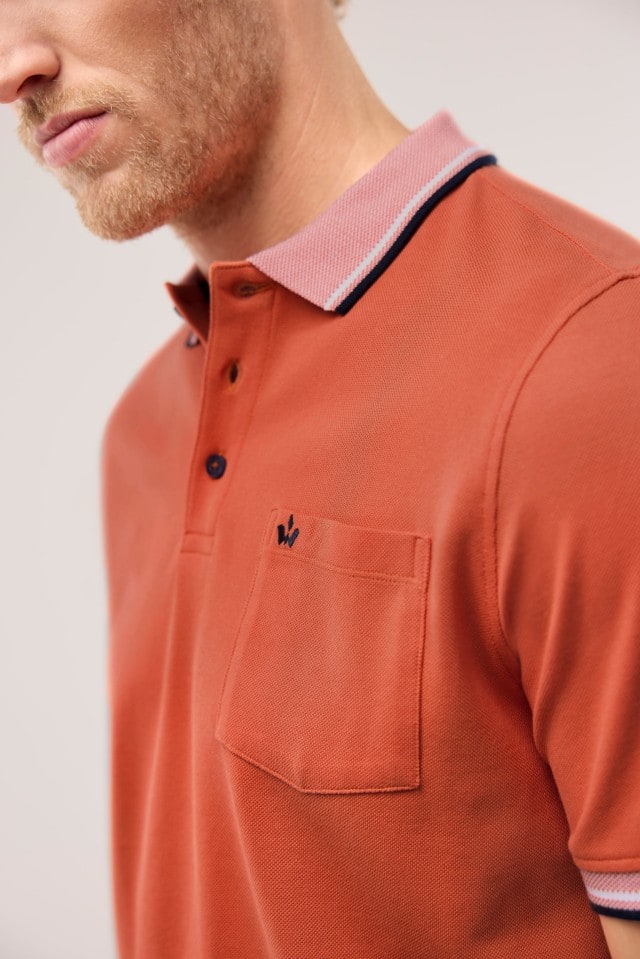 Ein Mann trägt ein Pique-Polo Hitzefrei in Uni Orange.