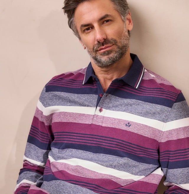 Ein Mann mit grauen Haaren und Bart trägt ein langärmliges, gestreiftes Poloshirt in Blau-, Violett- und Weißtönen und schaut entspannt in die Kamera. Ein Mann mit grauen Haaren und Bart trägt ein langärmliges, gestreiftes Poloshirt in Blau-, Violett- und Weißtönen und schaut entspannt in die Kamera.