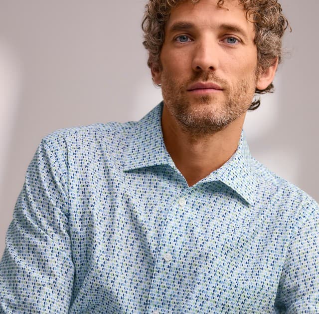 Eine Person mit lockigem Haar trägt ein hell gemustertes Hemd und blickt ruhig in die Kamera.