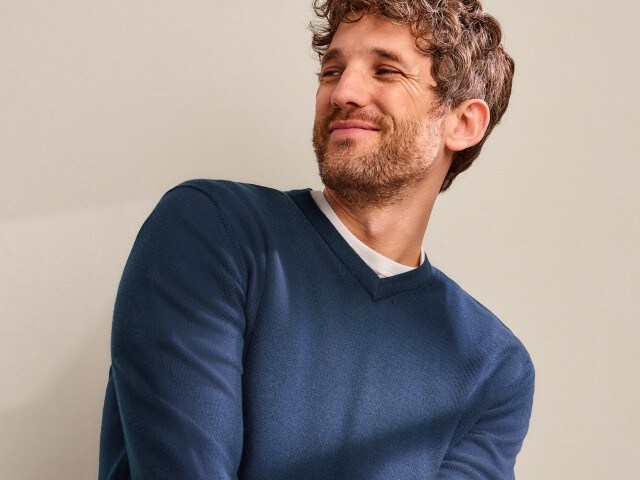 Ein Mann trägt einen dunkelblauen Pullover mit V-Ausschnitt und schaut zur Seite. 