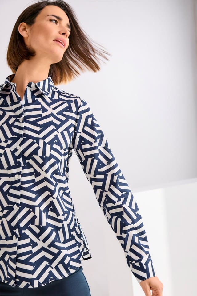 Eine Person mit kinnlangem Haar trägt ein dunkelblau-weiß gemustertes Hemd und bewegt den Kopf dynamisch zur Seite.