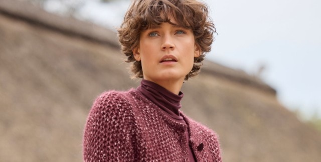 Eine Person trägt eine weinrote Strickjacke über einem Rollkragenpullover. Der Look wirkt warm, gemütlich und elegant.