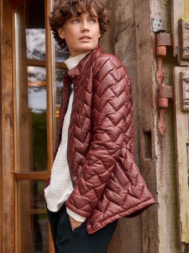Eine Frau trägt eine gesteppte, weinrote Lederjacke über einer weißen Bluse. Der Look wirkt stilvoll, modern und herbstlich.