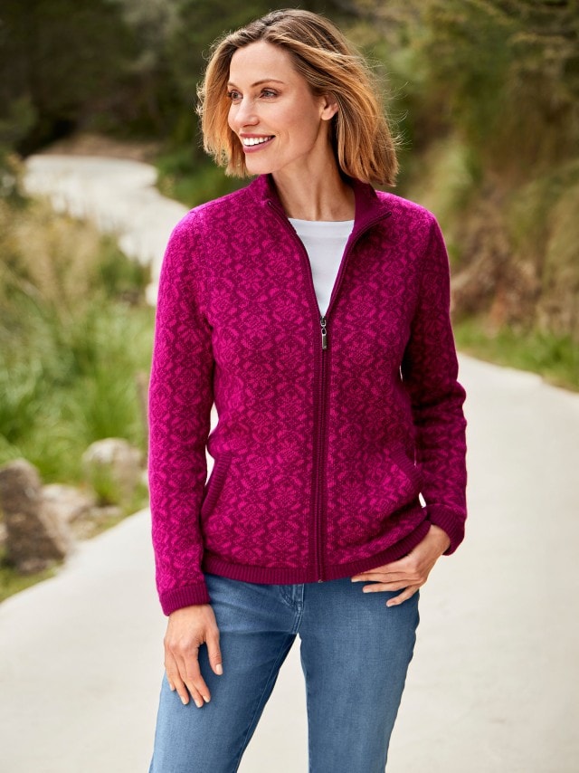 Frau in einer beerefarbenen Strickjacke und Jeans steht auf einem Wanderweg.
