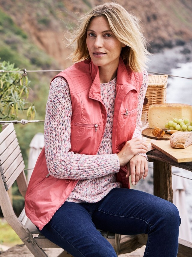 Frau in einer lachsfarbenen Weste und einem gemusterten Pullover sitzt an einem Picknicktisch.