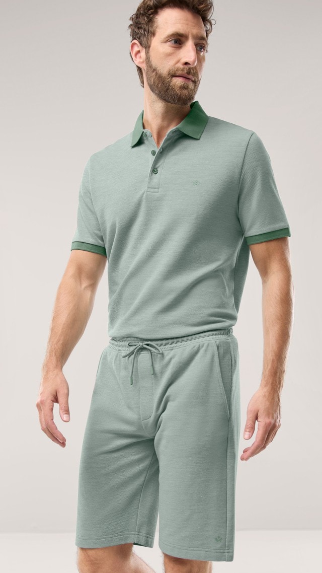 Ein Mann trägt ein Freizeitpolo Extraglatt in Salbei, dazu die passende Freizeitshorts Extraglatt.