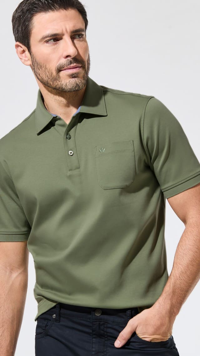 Ein Mann trägt ein olivgrünes Poloshirt mit Brusttasche und dunkle Hose. Der Stil ist sportlich-elegant und vielseitig kombinierbar.