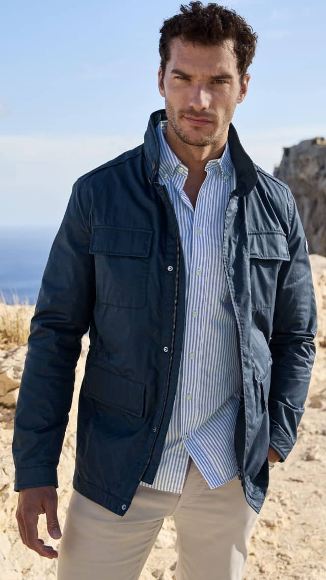 Ein Mann steht in einer hellen Felsenlandschaft und trägt eine dunkelblaue Jacke über einem gestreiften Hemd. Ein Mann steht in einer hellen Felsenlandschaft und trägt eine dunkelblaue Jacke über einem gestreiften Hemd.