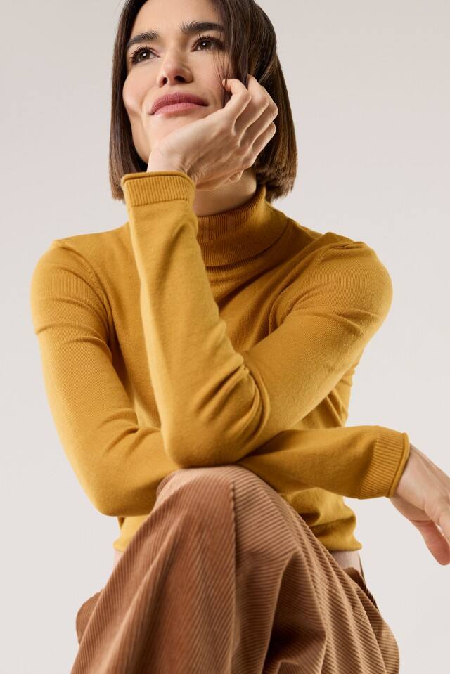 Eine Frau trägt einen Viskose-Rolli in Safran, dazu eine Cord-Hose in Beige.