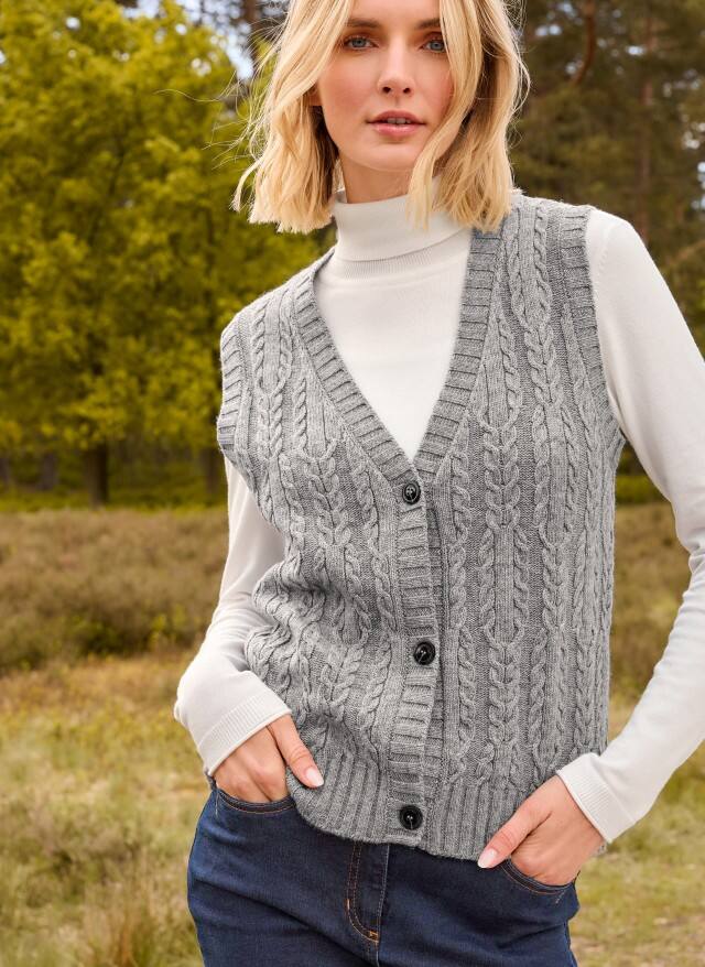 Eine Frau trägt einen weißen Rolli, darüber eine Strickweste in grau und dazu eine Jeans. Eine Frau trägt einen weißen Rolli, darüber eine Strickweste in grau und dazu eine Jeans.