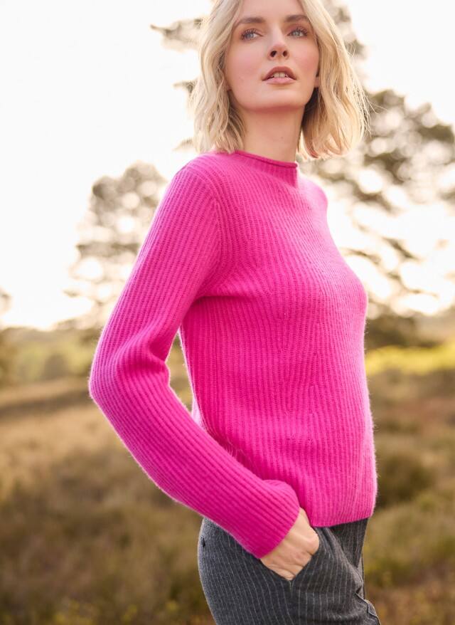 Eine blonde Frau trägt einen Cashmere Pullover in Fuchsia, dazu eine Jeans. Eine blonde Frau trägt einen Cashmere Pullover in Fuchsia, dazu eine Jeans.