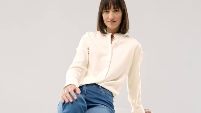Eine Frau vor einem neutralen Hintergrund trägt die Easy Care Crincle Bluse in Offwhite, dazu eine hellblaue Jeans.