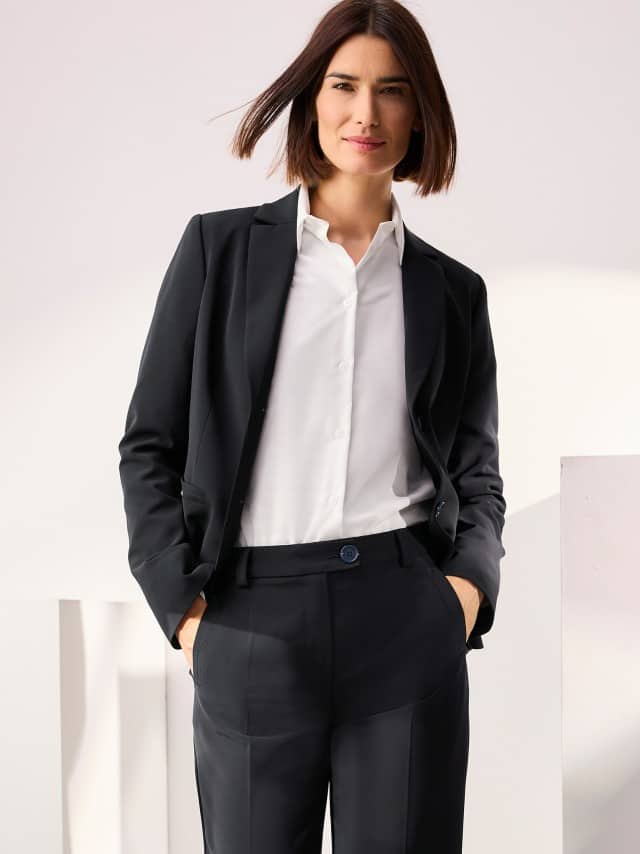 Frau trägt einen schwarzen Hosenanzug mit weißer Bluse – klassischer, eleganter Business-Look.