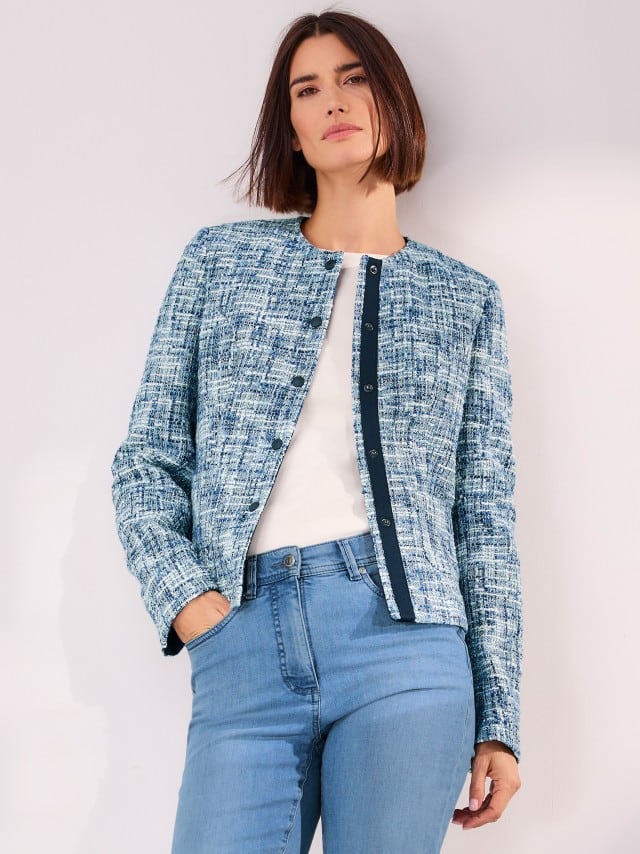 Frau trägt eine blau-weiß gemusterte Jacke in Tweed-Optik über einem weißen Shirt und hellblauer Jeans – moderner, lässig-eleganter Look.