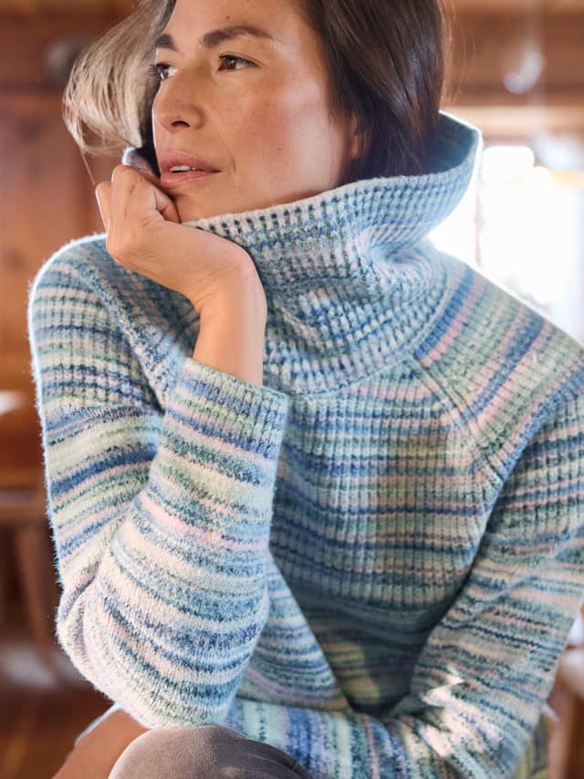 Eine Frau sitzt in einer Holzhütte und trägt einen Softcotton Rolli Icecolors, hält den Kragen und schaut zur Seite.