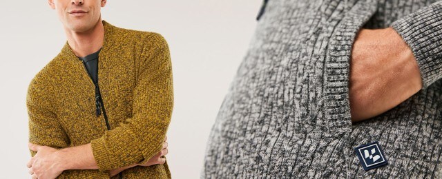 Ein Mann trägt eine grob gestrickte Strickjacke in Senfgelb, daneben ist eine ähnliche Strickjacke in Grau zu sehen. Die Strickjacken wirken gemütlich und modern.