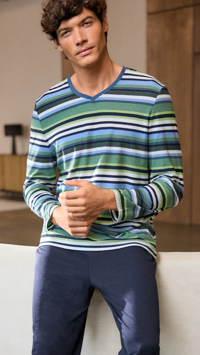 Dunkelhaariger Mann stehend vor einer Couch in blau/grünem Cooling Pyjama