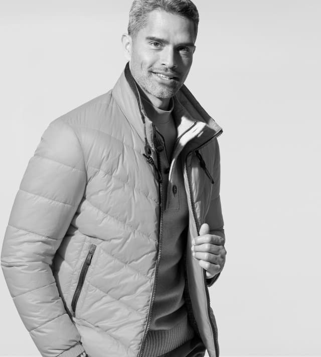 Ein Mann trägt eine gesteppte Jacke über einem Pullover und Hemd. Sein Stil wirkt sportlich-elegant und für kühle Tage geeignet.