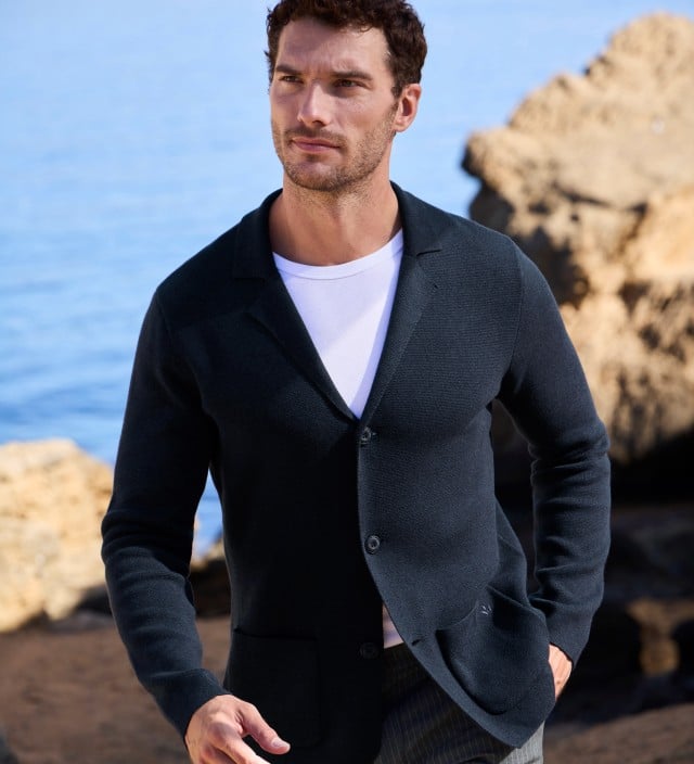 Ein Mann trägt eine dunkelblaue Strickjacke über einem weißen T-Shirt. Sein Stil wirkt lässig, elegant und perfekt für den Frühling.