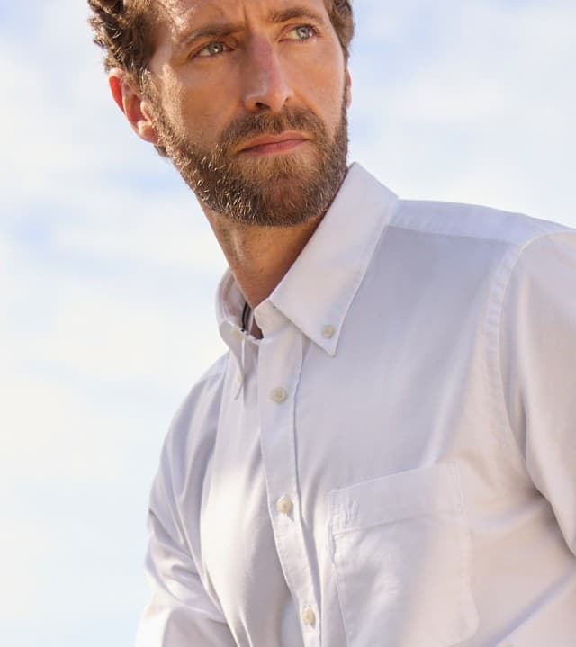 Ein Mann trägt ein weißes Hemd und schaut in die Ferne.