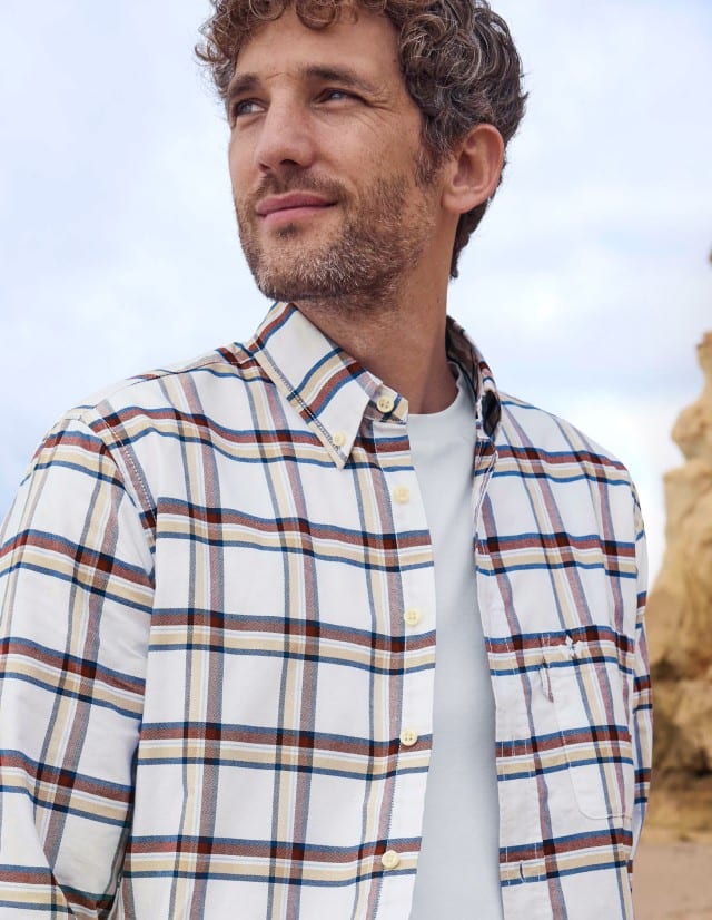 Eine Mann trägt ein lässiges, mehrfarbig kariertes Hemd über einem weißen Shirt, was entspannt, freundlich und natürlich wirkt.