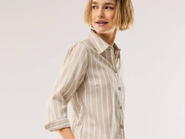 Eine Frau trägt eine gestreifte Leinenbluse in Beige.