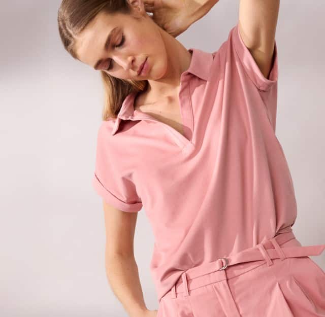 Eine Frau trägt ein Poloshirt in Rosa, dazu die passende Hose.