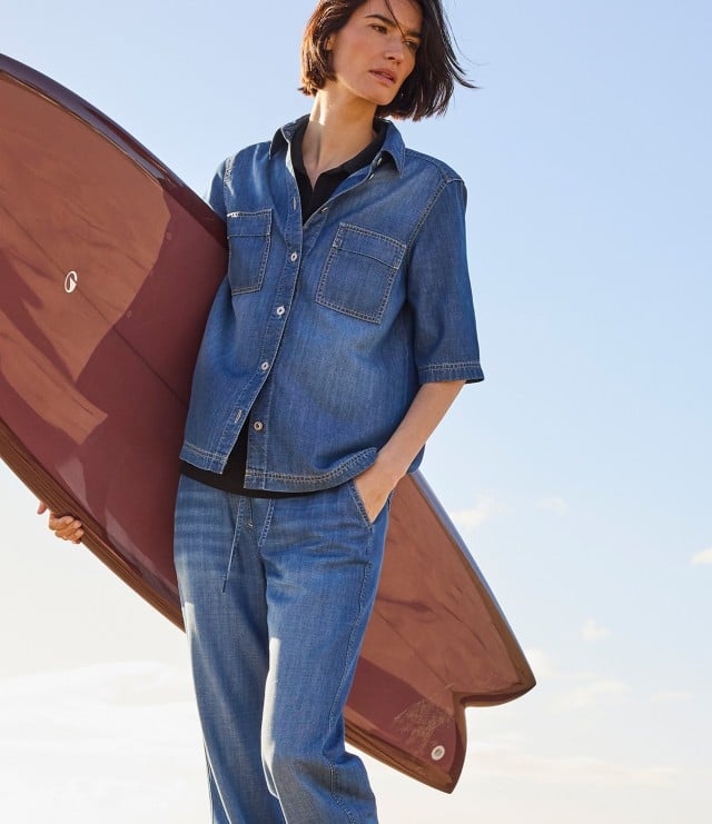 Person trägt ein legeres Denim-Outfit aus Jeanshemd und Jeanshose im Freizeitstil.