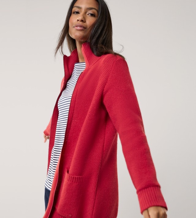 Ein Frau trägt einen rote Strickjacke mit Reißverschluss, darunter ein gestreiftes Shirt. 