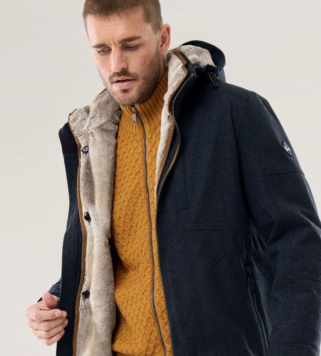 Ein Mann trägt die Aquastop Winterjacke in Marine, darunter einen Strickcardigan in Senfgelb.