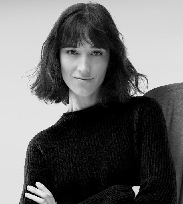 Ein dunkelhaarige Frau trägt einen schwarzen Strickpullover mit Stehkragen, ein Mann trägt einen dunklen Cardigan mit einem hellen Shirt darunter.