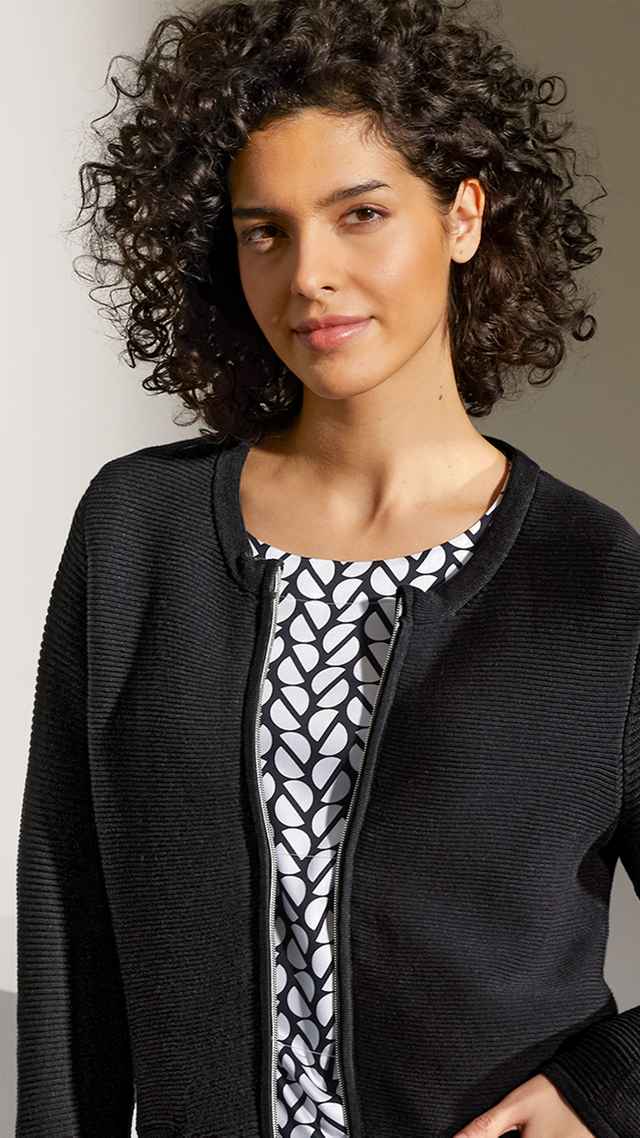 Eine Dame mit einer schwarzen Reißverschlussjacke und einer schwarz weißen Bluse darunter