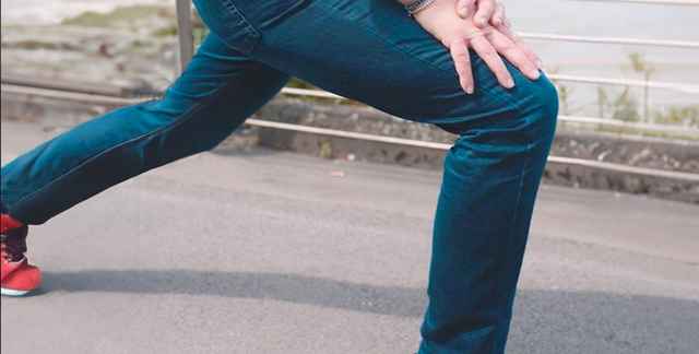 Person dehnt ihr Bein in blauer Joggerjeans auf einer Straße.