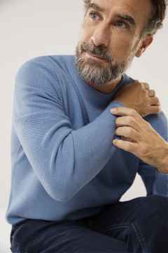 Ein Mann trägt einen leichten blauen Pullover, dazu eine Jeans.