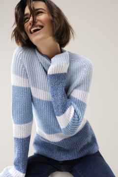 Eine Frau trägt einen Strickpullover mit Streifen, dazu eine Jeans.