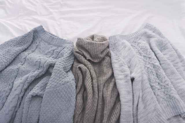 Drei Pullover, die zum Trocknen auf einem Bett liegen.