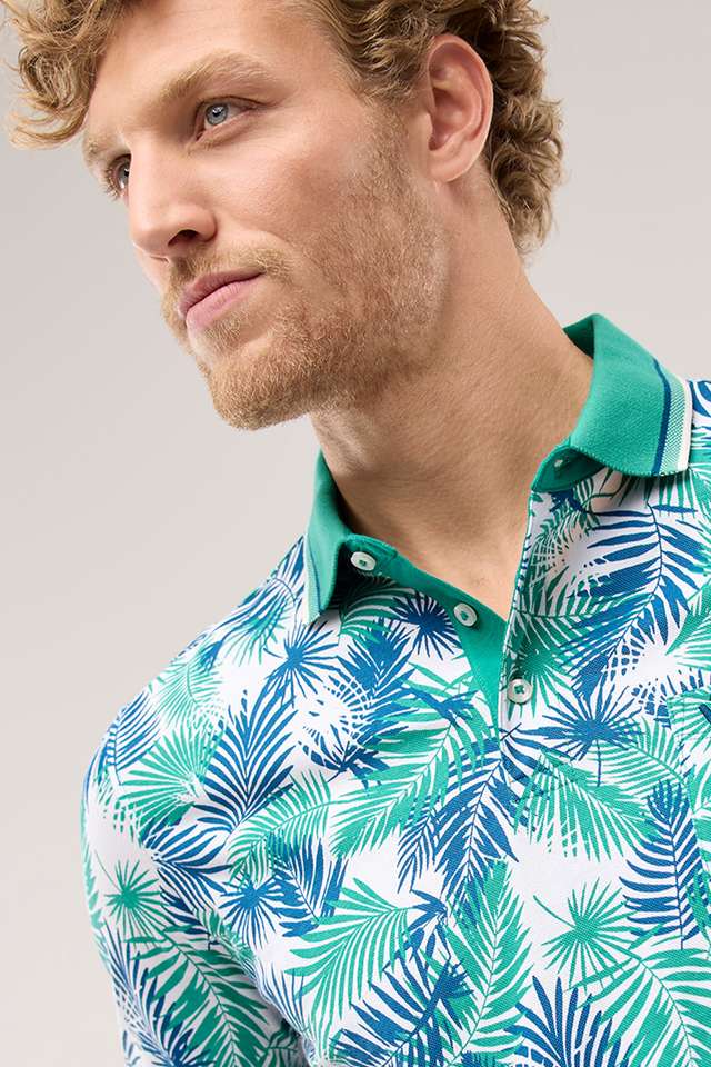 Mann mit lockigem Haar trägt ein buntes Polohemd mit tropischem Blätterdesign und eine weiße Hose. Angezeigt beim Hover
