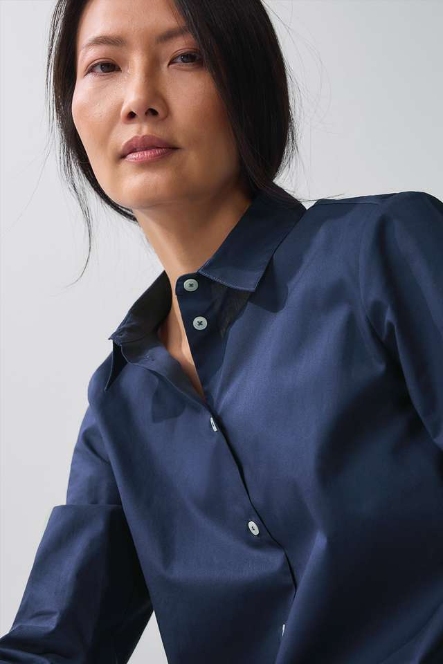 Eine Person mit langen Haaren trägt ein blaues Hemd und eine blaue Jeans, blickt zur Seite, die Hände in den Hosentaschen. Angezeigt beim Hover