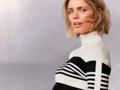 Frau mit kurzen blonden Haaren trägt einen gestreiften Pullover vor grauem Hintergrund.