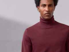 Person mit dunkelrotem Rollkragenpullover vor grauem Hintergrund.